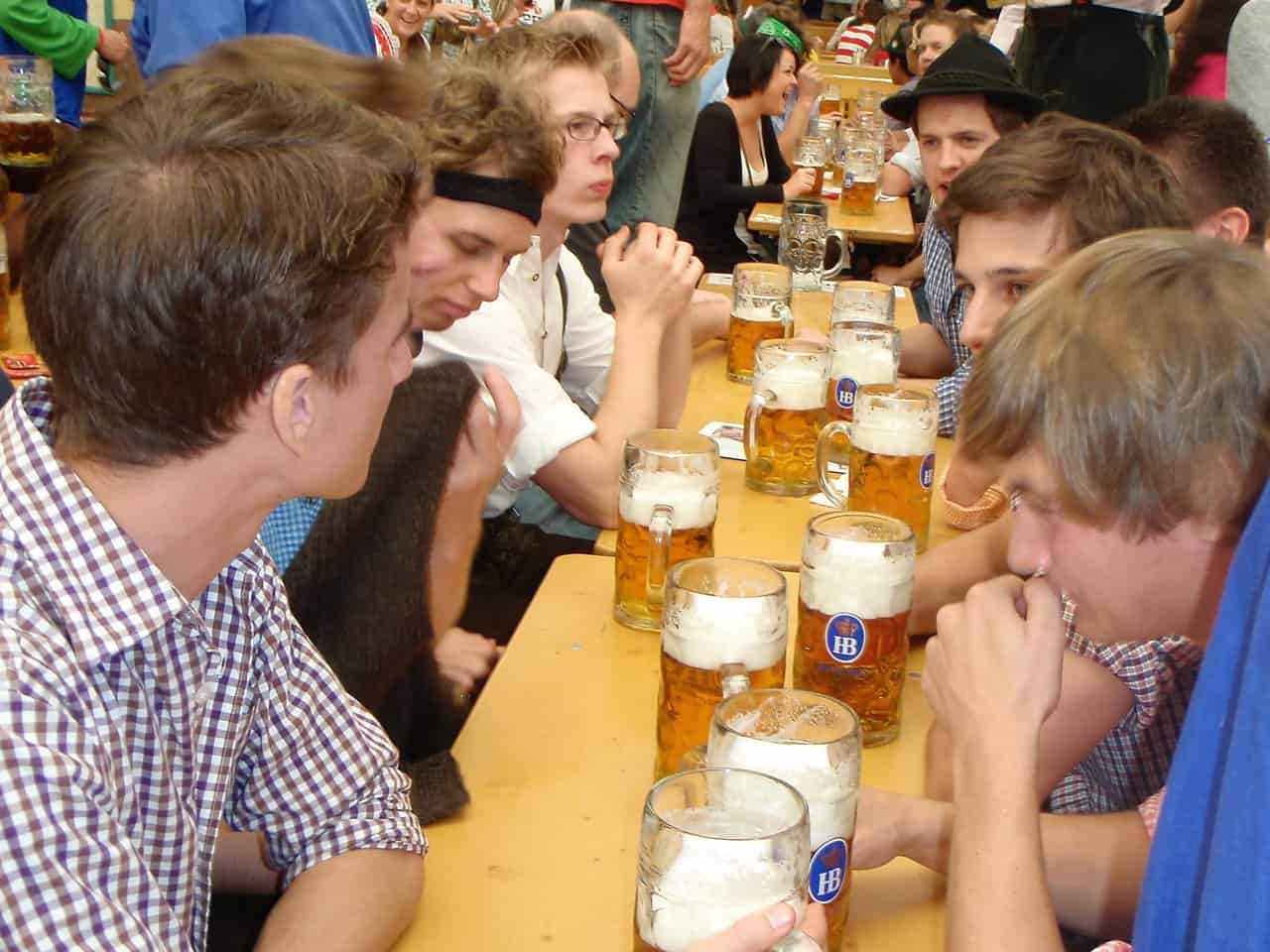 Young men seated at long wooden tables with large beer mugs during Oktoberfest celebration