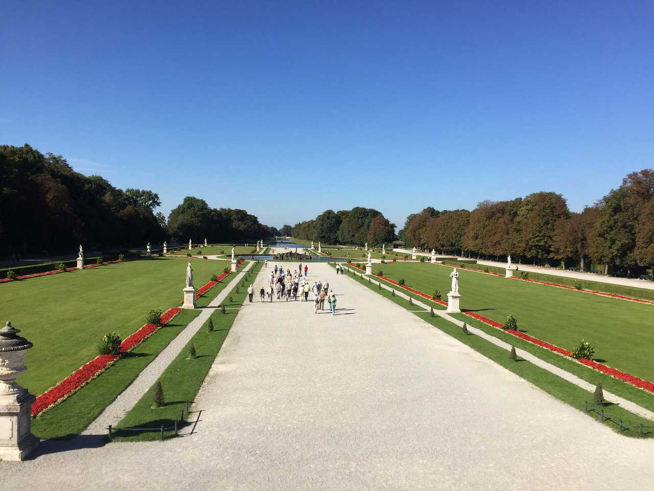 Wide view of formal baroque garden with statues and gravel path at Nymphenburg Palace in Munich