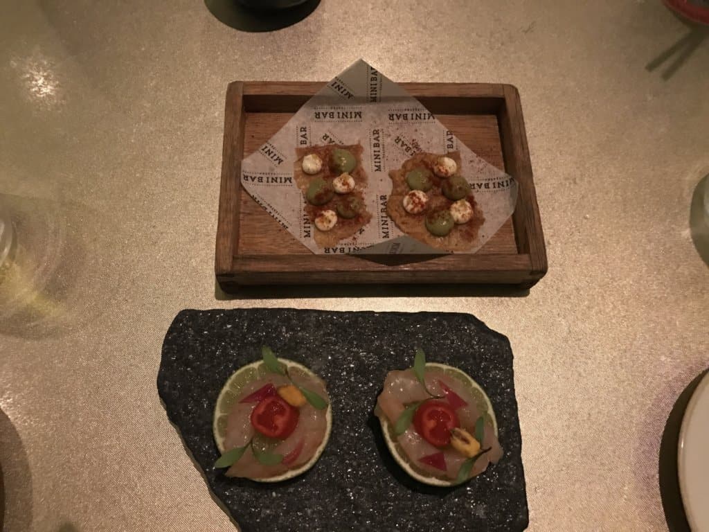 Two gourmet tapas dishes featuring miniature tacos and citrus-based appetizers, plated on wood and stone