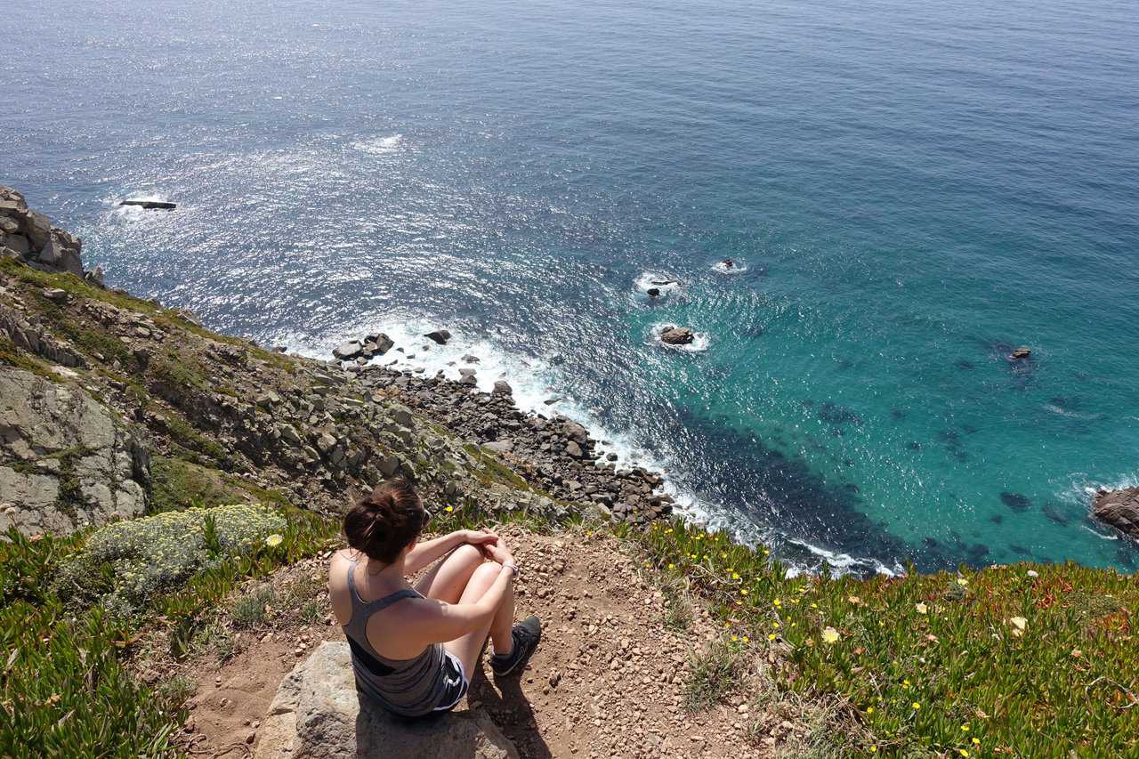 Woman sitting on a cliff at Cabo da Roca, gazing at the rocky Atlantic coastline below