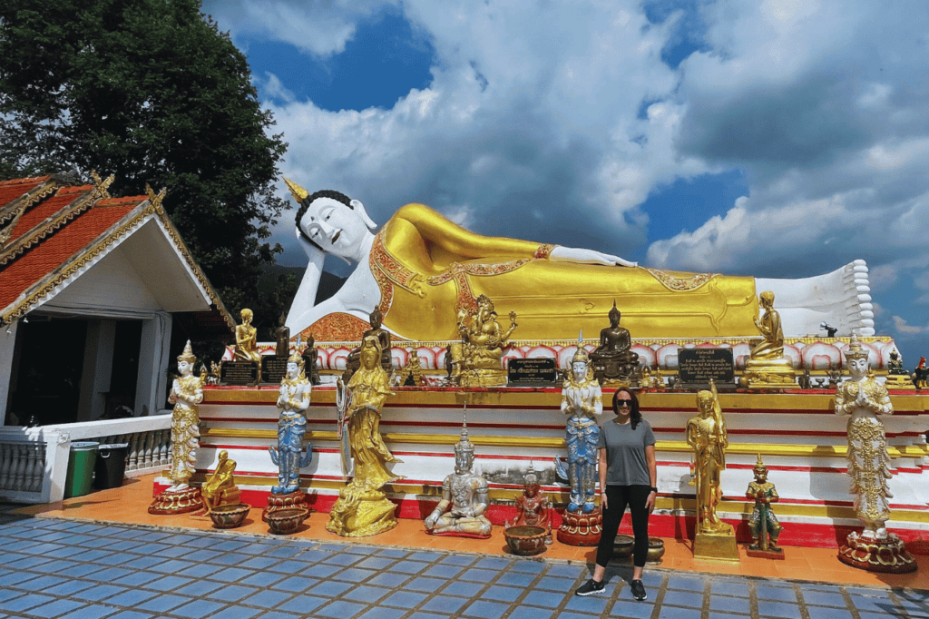 woman standing in front of a reclining buddha at wat phra that doi kham in chiang mai