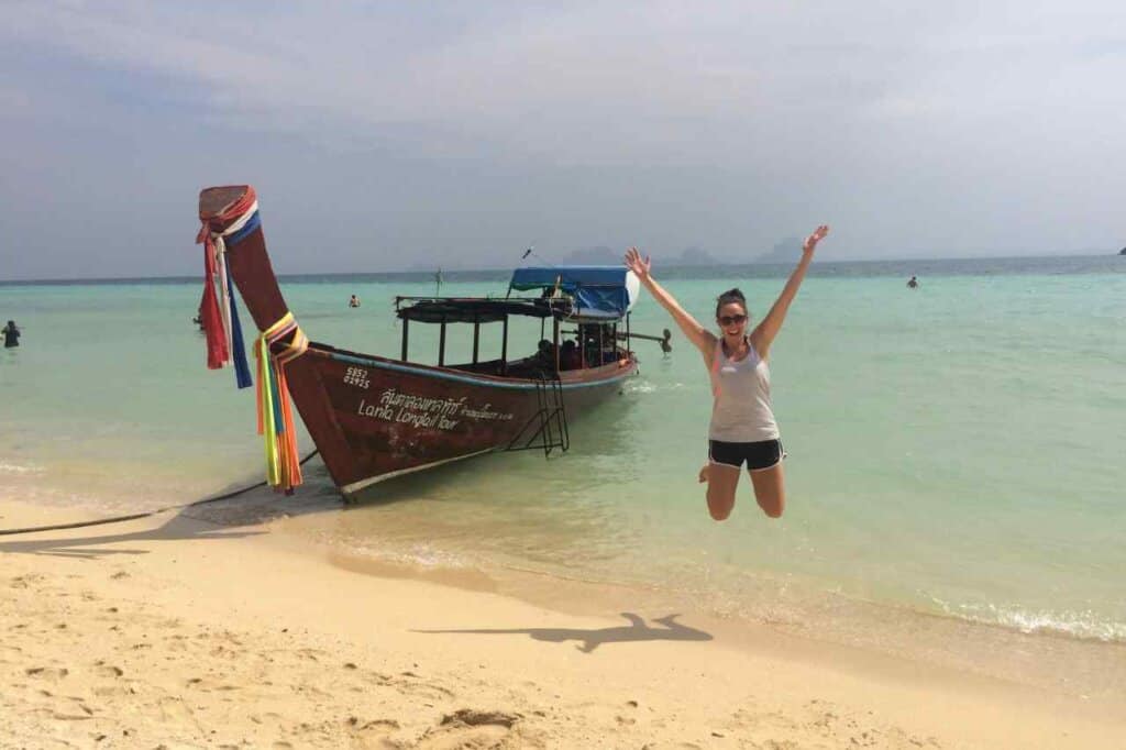 woman jumping up in front of a longtail boat during her Thailand travel itinerary 