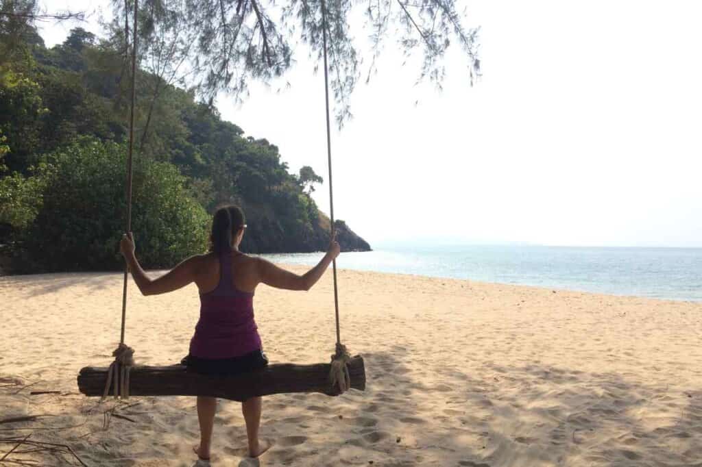 woman sitting on a swing looking at the beach during her thailand travel itinerary