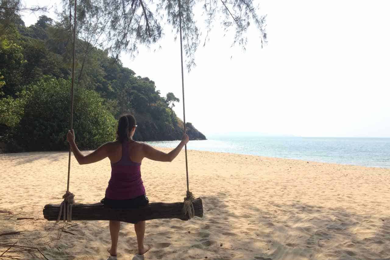 woman sitting on a swing looking at the beach in thailand