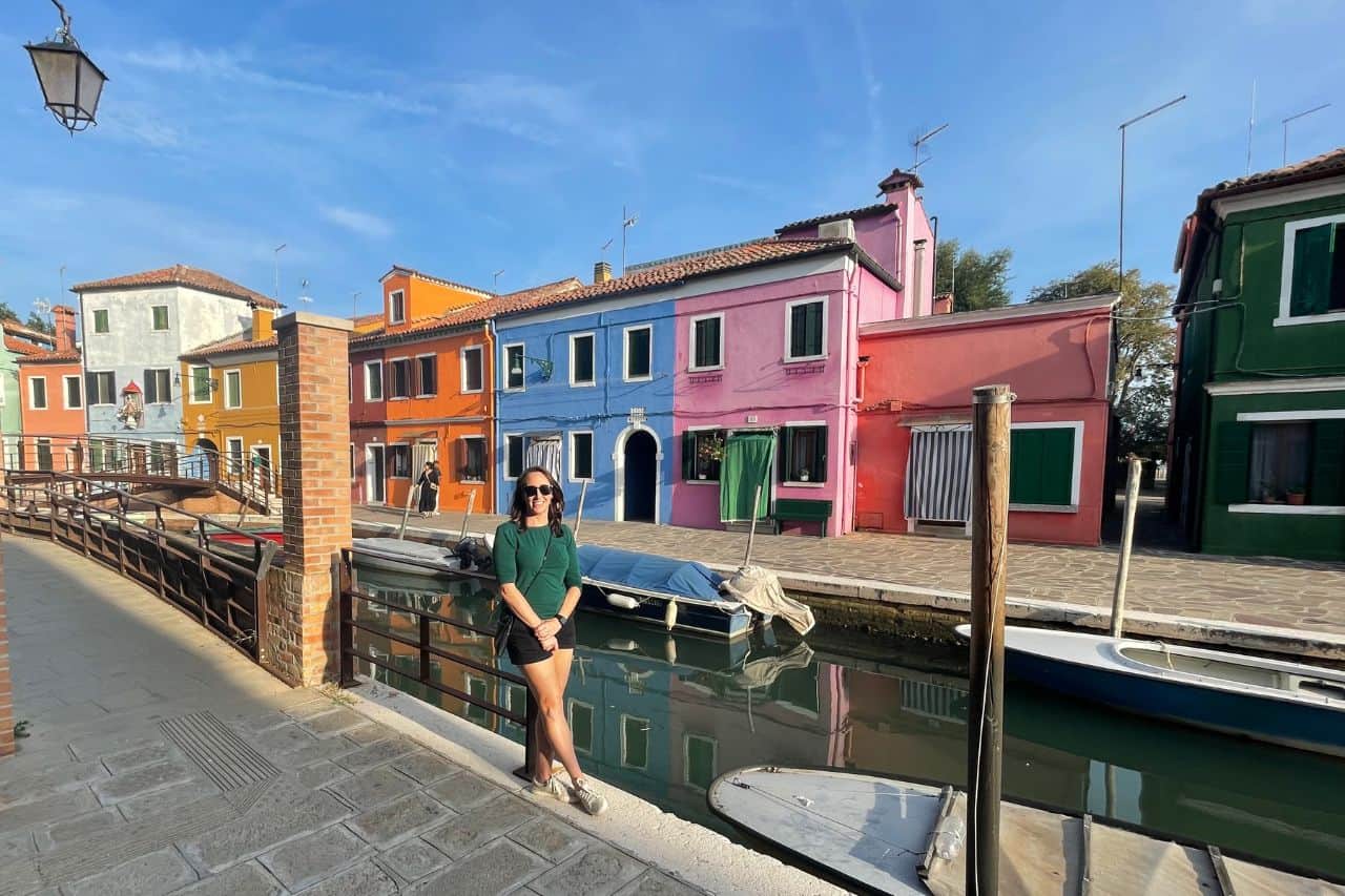 woman standing next to a dock filled with colorful homes in Burano Italy