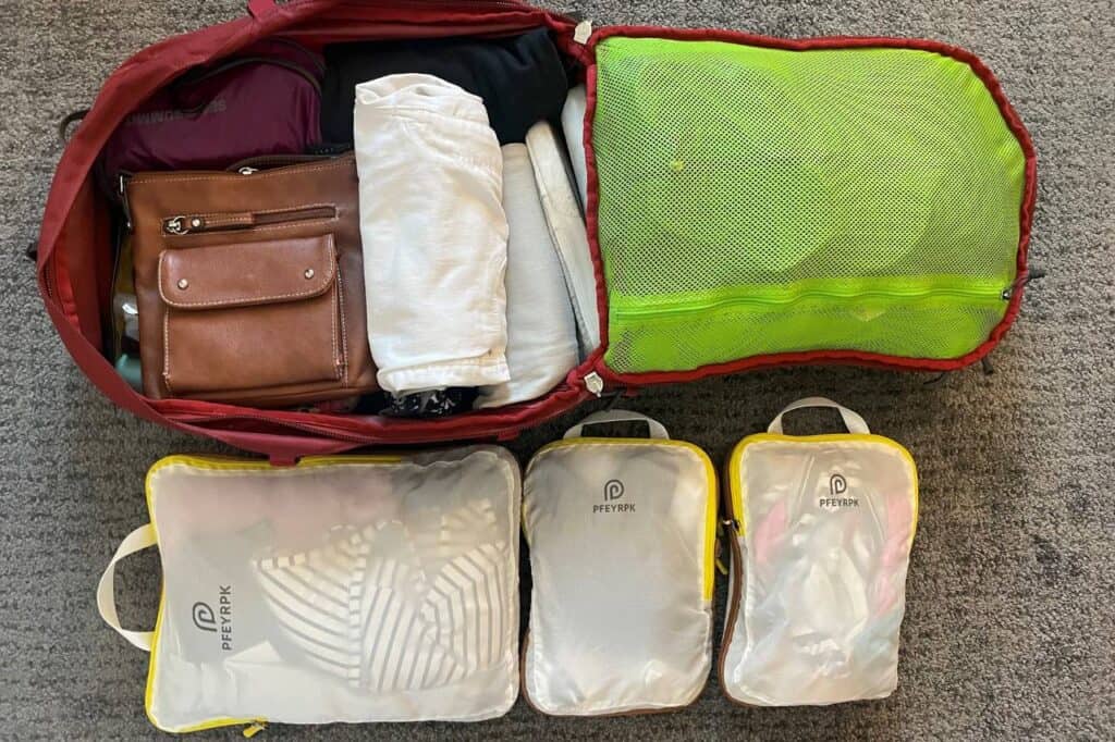 red backpack partially packed with packing cubes next to it