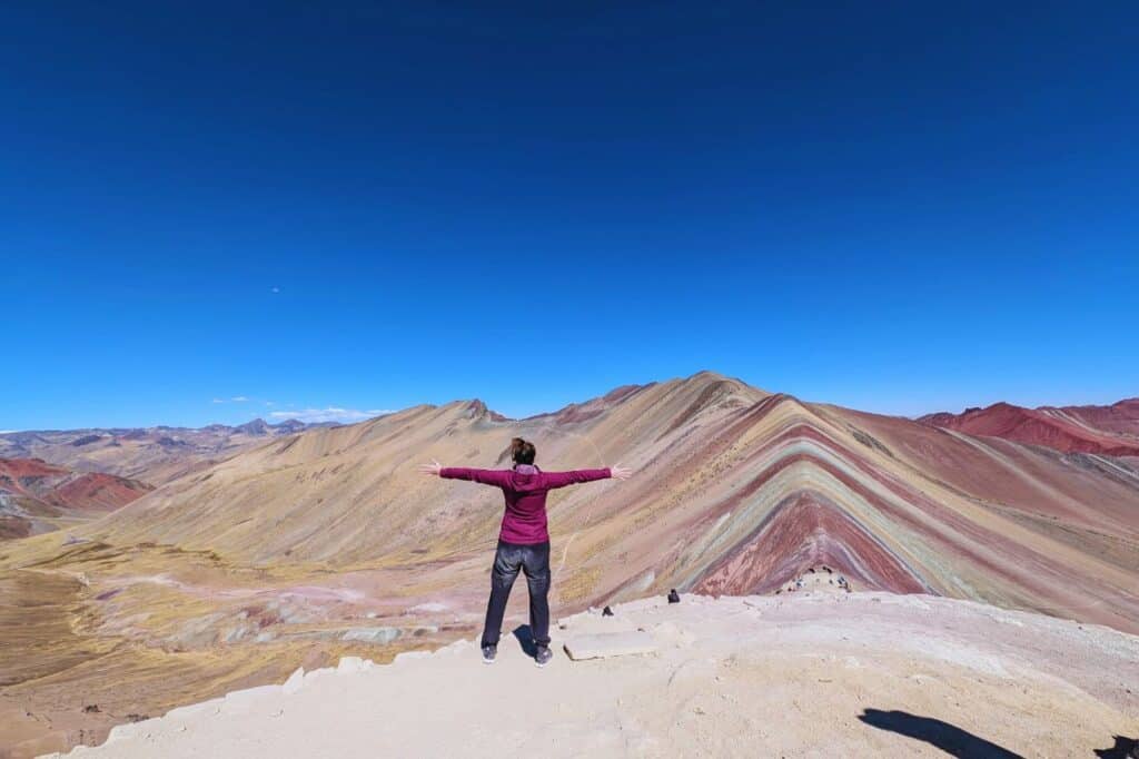 woman with her arms wide open on top of rainbow mountain