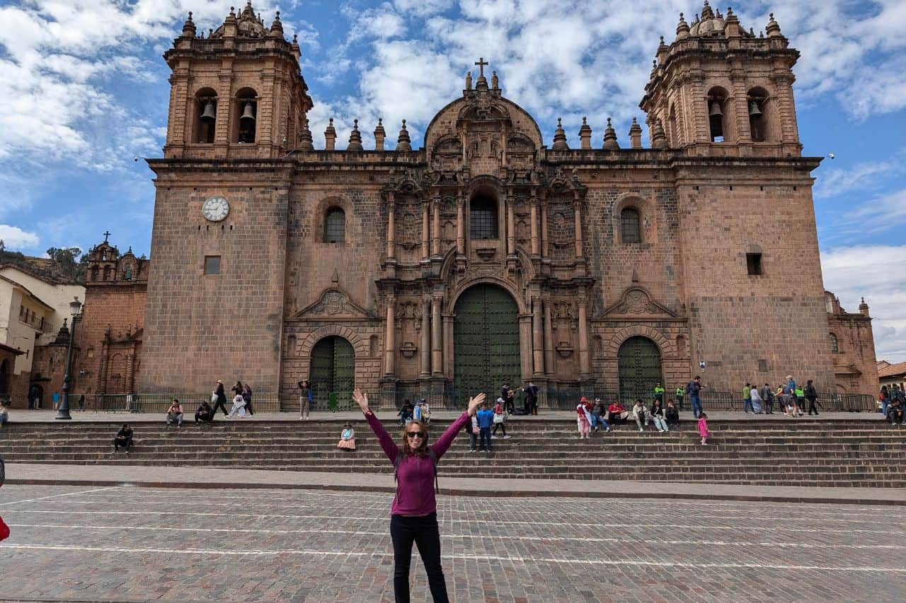 woman with her hands up in front of a church in cusco - best travel websites