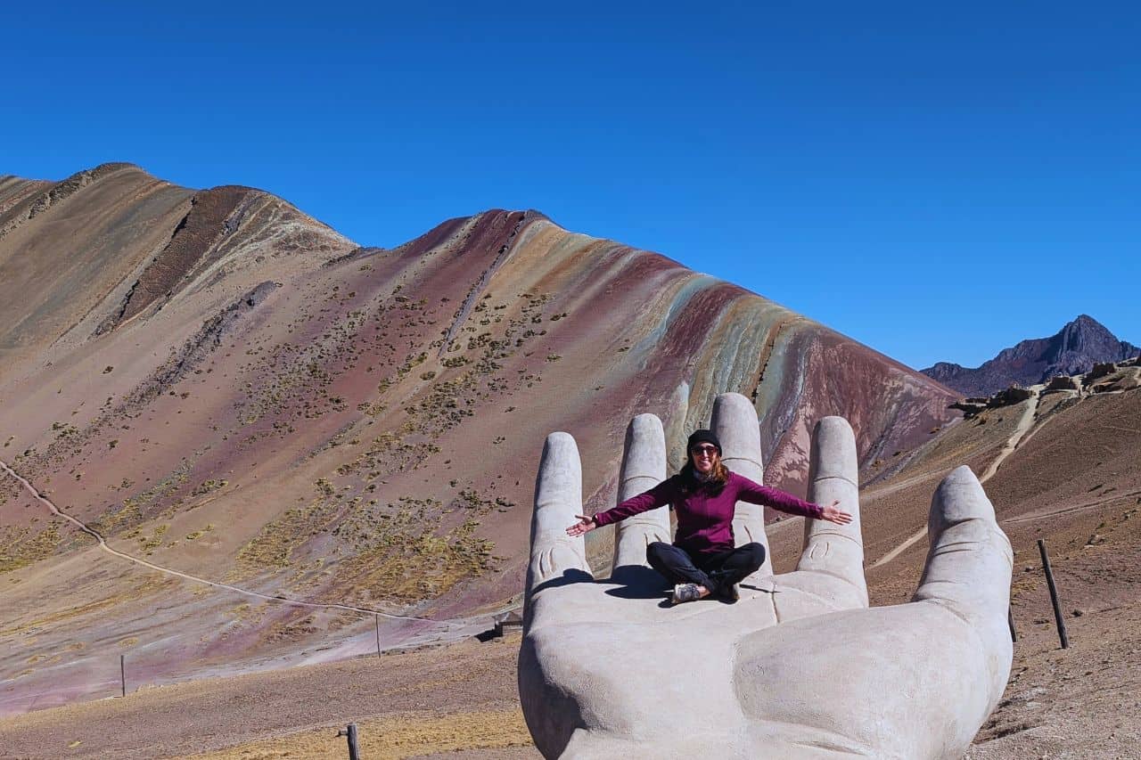 woman sitting on a giant marble hand at rainbow mountain