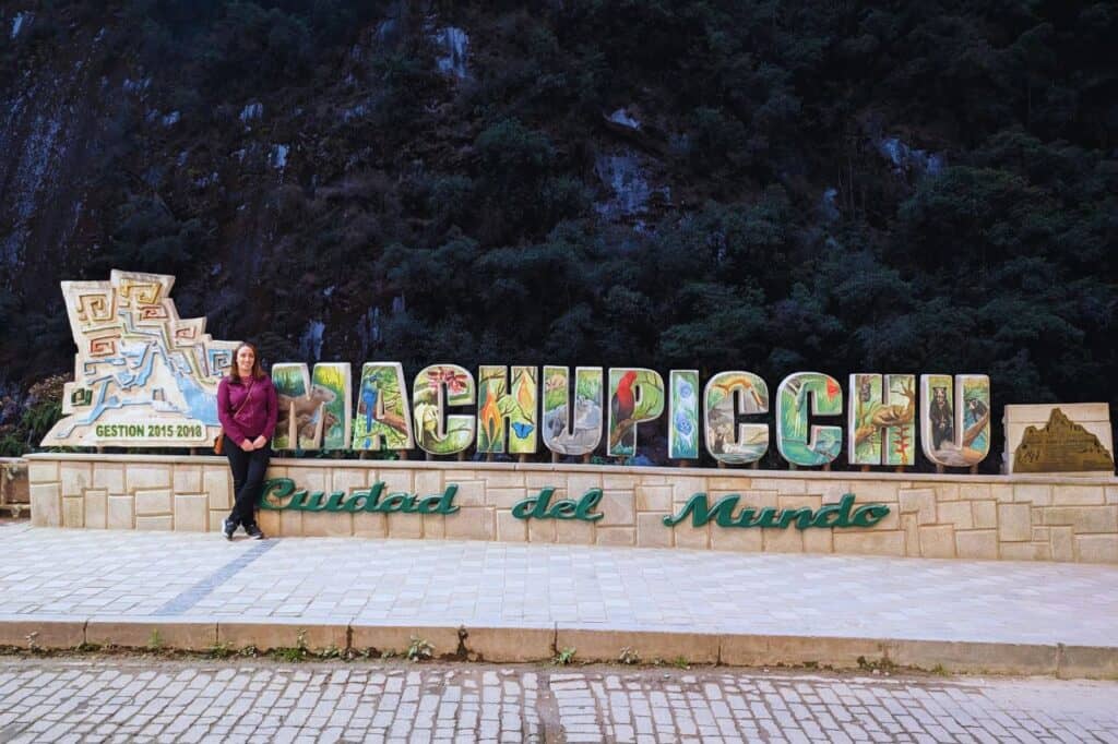 woman standing in front of a machu pichhu sign in aguas calientes