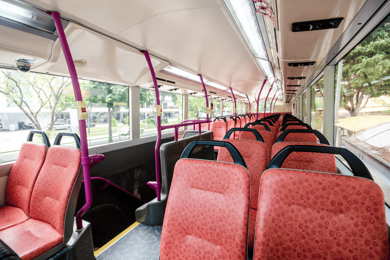 The interior of a bus with red seats and entertainment screens for bus travel from Singapore to Kuala Lumpur.