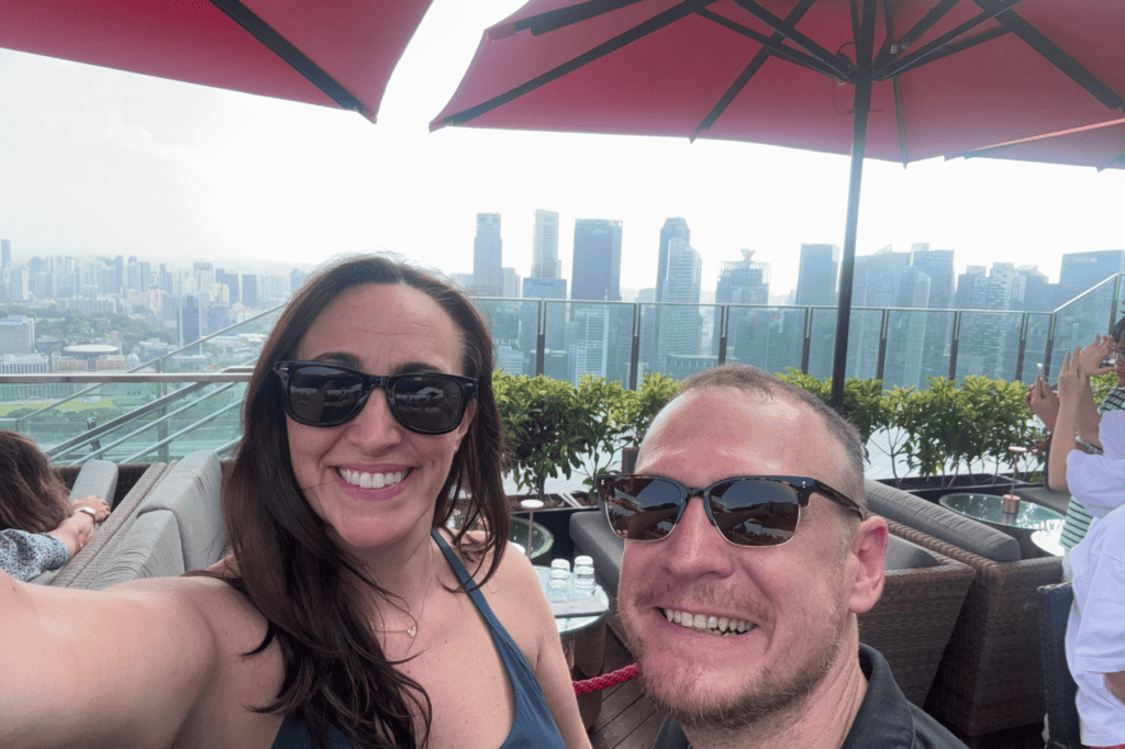 Two people taking a selfie on the Ce La Vi rooftop with the Singapore skyline in the background