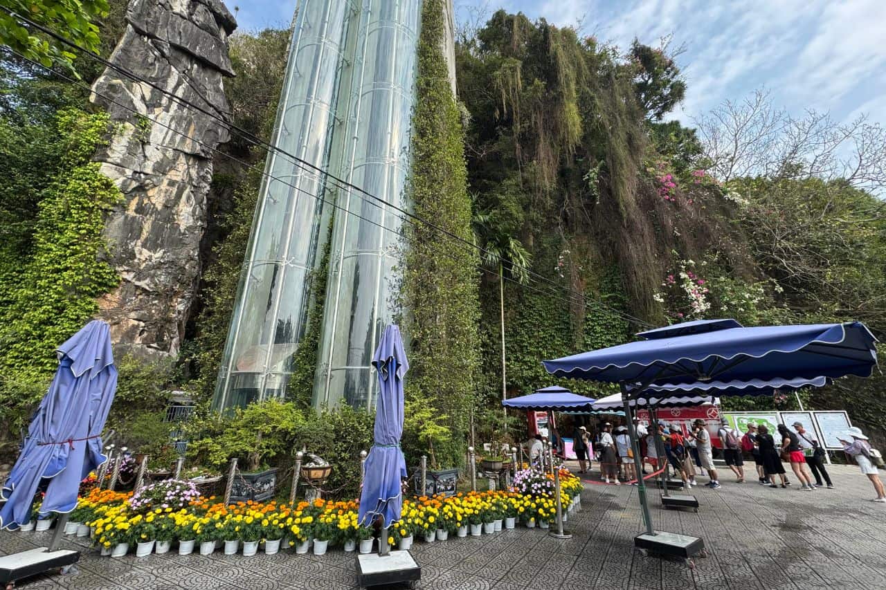 Glass elevator shafts surrounded by greenery and tourists at the base of Marble Mountains Vietnam
