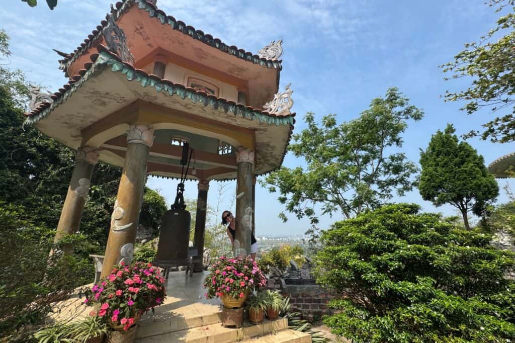 Traditional bell tower pavilion surrounded by flowers with Da Nang view at Marble Mountains Vietnam