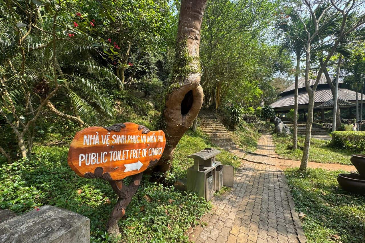 Wooden sign for free public toilets along a leafy path in Marble Mountains Vietnam