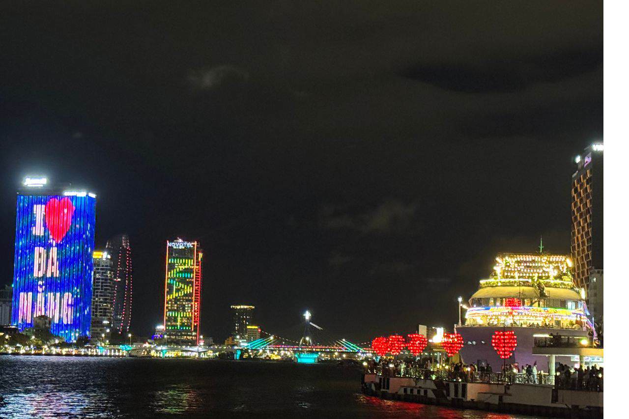 Night view of Da Nang skyline with colorful lit buildings and the Love Bridge adorned with red heart lanterns
