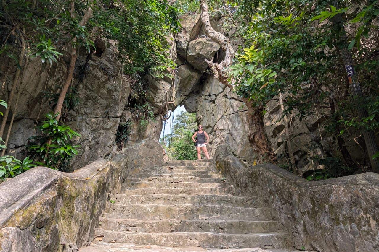 Tourist standing under a dramatic natural rock arch along stone stairs at Marble Mountains Vietnam