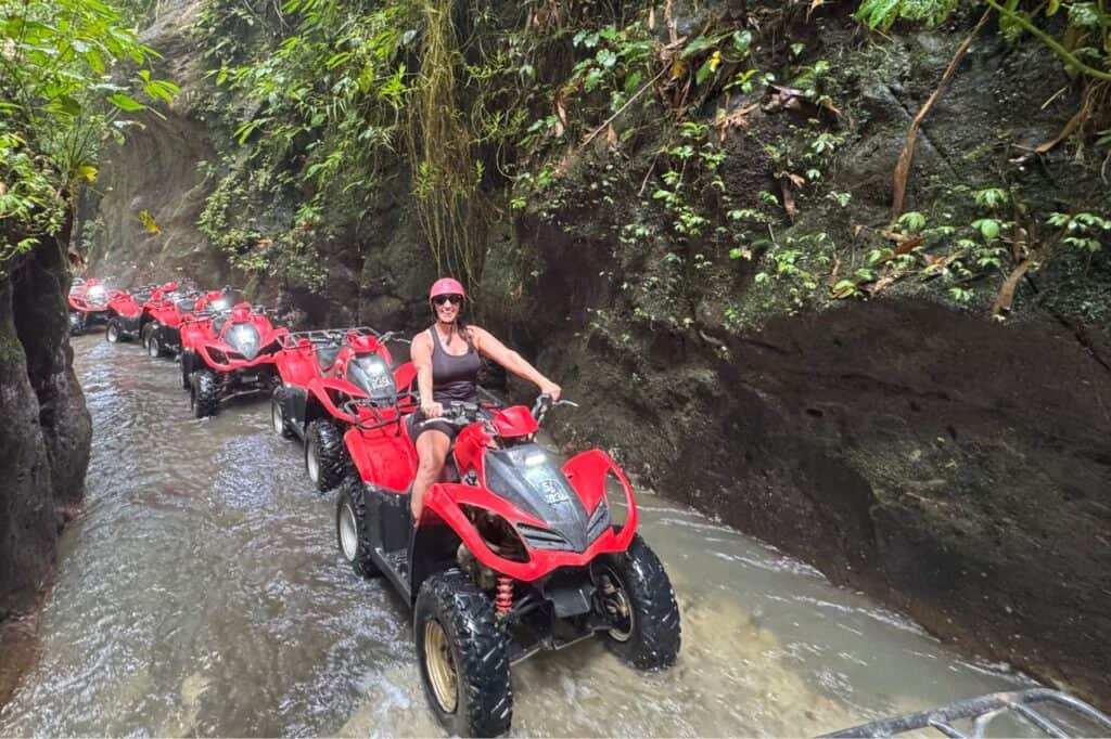 A group of people riding red ATVs through a narrow water-filled canyon in the jungle of Bali.