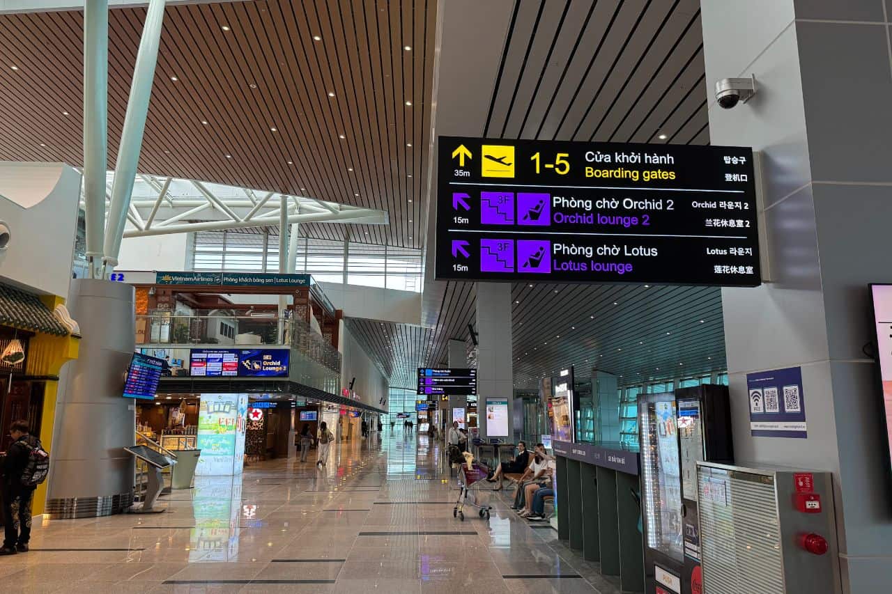 Digital departure board above check-in counters at Da Nang Airport, showing flight details and gate information