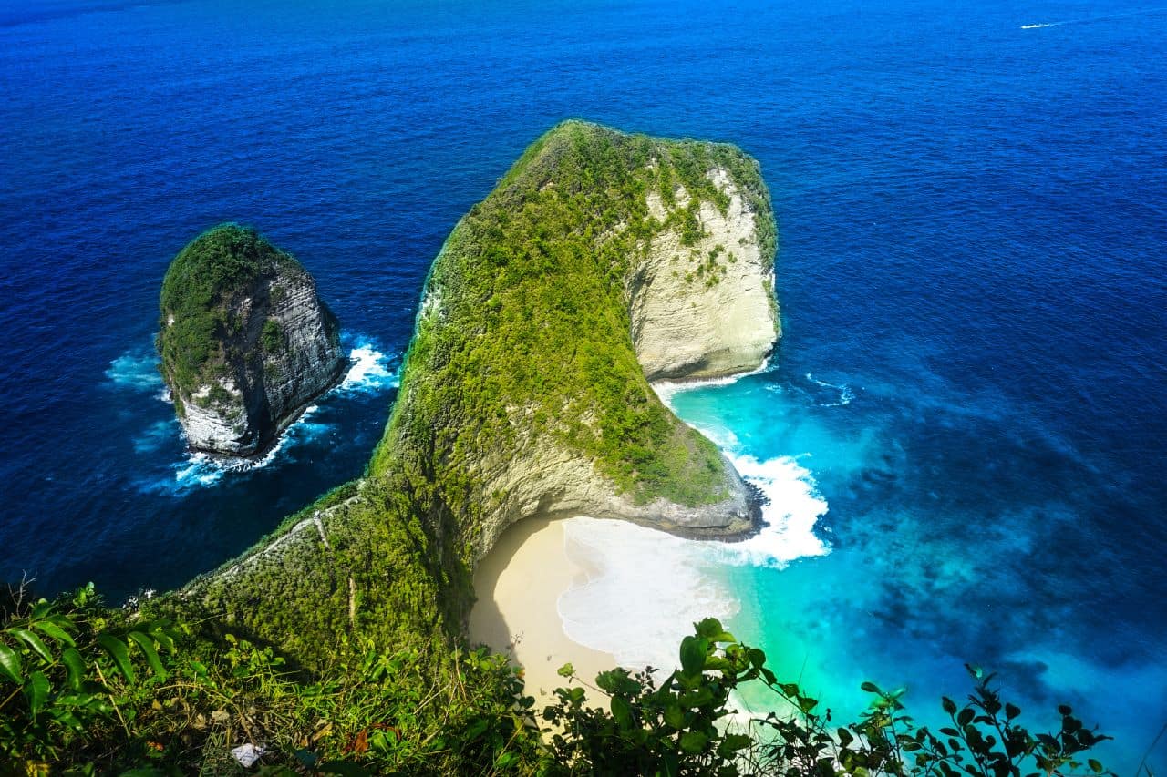 Famous cliffs and beach at Nusa Penida with deep blue ocean waves crashing on the shore.