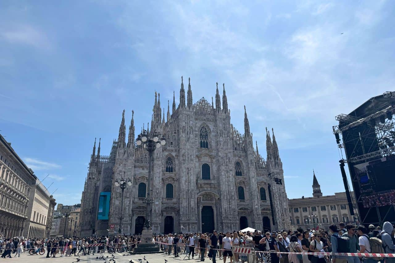 Front View of the Milan Cathedral in Piazza del Duomo Crowd gathered in front of the Milan Cathedral with its gothic spires and detailed stone facade under a clear blue sky