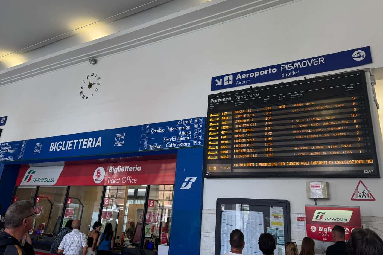 Digital train departure board at Pisa Centrale station showing schedules and destinations on screen