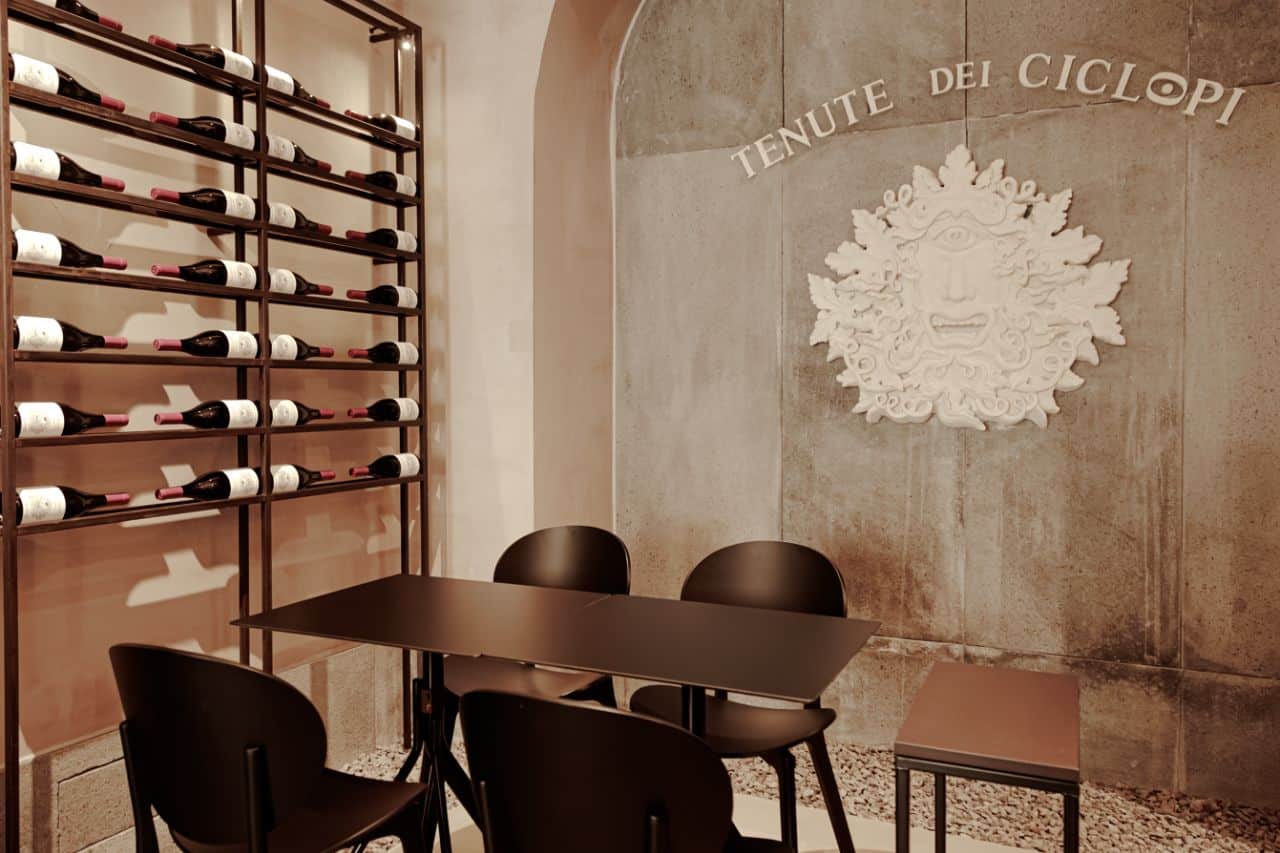 Tenute dei Ciclopi Wine Tasting Room in Catania Seating area inside the Tenute dei Ciclopi wine tasting room in Catania with Etna wine bottles displayed on the wall.