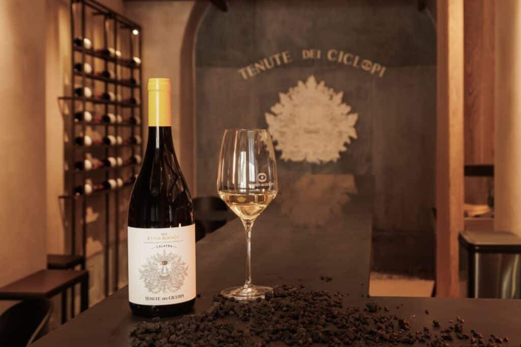 A bottle of Etna Bianco and a wine glass inside the Tenute dei Ciclopi wine tasting room in Catania, Sicily.